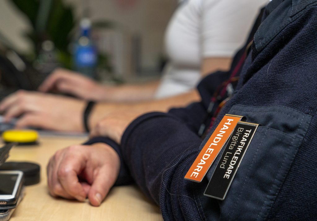 Underarmar och händer på ett skrivbord. På en ärm syns en skylt med texten handledare