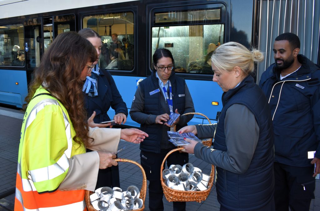Fem personer framför en ljusblå spårvagn med reflexer i små korgar.
