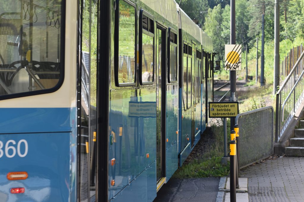 En blå-vit spårvagn vid en spårvagnshållplats.